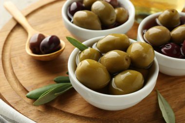 Lezzetli zeytinler tabakta, kaşık ve yeşil yapraklar masada, yakın plan.