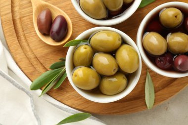 Lezzetli salamura edilmiş zeytinler kaseler, kaşık ve yeşil yapraklar gri masada, üst manzara