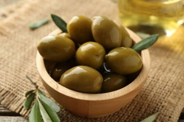 Lezzetli marine edilmiş zeytinler kasede ve yeşil yapraklar masada, yakın plan.