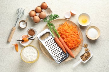 Bej desenli masa üzerinde havuçlu kek yapmak için farklı malzemeler.