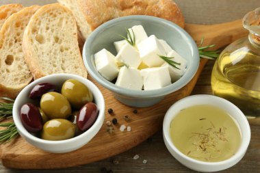 Ahşap masada servis edilen lezzetli marine edilmiş zeytin, ekmek ve peynir, yakın plan.
