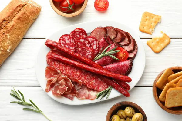 Farklı tütsülenmiş sosisler beyaz ahşap masada servis edilir.