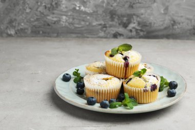 Yaban mersinli lezzetli kekler, pudra şekeri ve gri desenli masada nane şekeri, yakın plan. Metin için boşluk