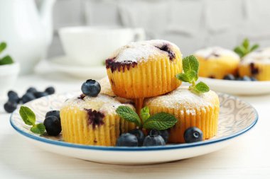 Yaban mersinli lezzetli kekler, pudra şekeri ve beyaz ahşap masada nane şekeri, yakın plan.
