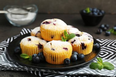 Yaban mersinli lezzetli çörekler, pudra şekeri ve nane şekeri siyah masada, yakın plan.