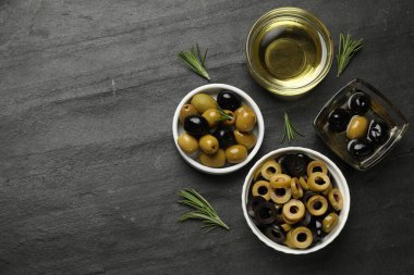 Farklı lezzetlerde marine edilmiş zeytin halkaları, bütün halkalar, koyu dokulu masa üzerinde yağ ve biberiye, düz yatak. Metin için boşluk
