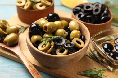 Farklı lezzetli marine edilmiş zeytin halkaları, hepsi ve biberiye açık mavi ahşap masada, yakın plan.