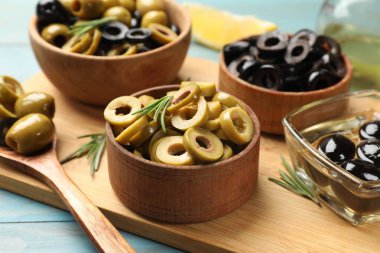 Farklı lezzetli marine edilmiş zeytin halkaları, tüm olanlar ve biberiye açık mavi ahşap masa, yakın çekim