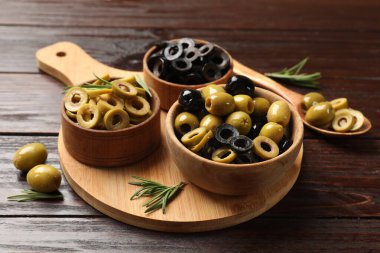 Farklı lezzetlerde marine edilmiş zeytin halkaları, tüm olanlar ve ahşap masada biberiye, yakın plan.