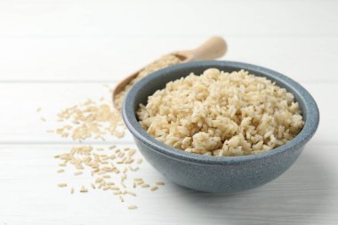 Lezzetli kahverengi pirinç kasede ve çiğ taneler beyaz ahşap masada, yakın plan.