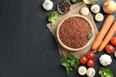 Tabaktaki çiğ kahverengi pirinç taze ürünlerin arasında koyu dokulu masada, düz yerde. Metin için boşluk