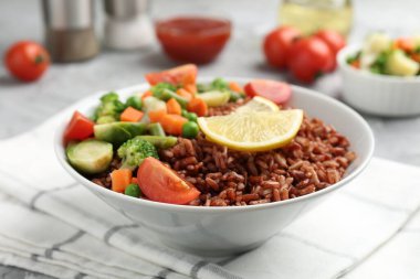 Gri masada servis edilen sebzeli ve limon dilimli lezzetli kahverengi pirinç, yakın plan.