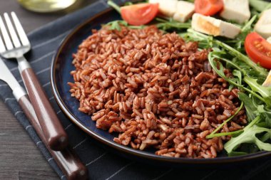 Lezzetli kahverengi pirinç, tavuk, roka ve domatesler siyah ahşap masada, yakın plan.