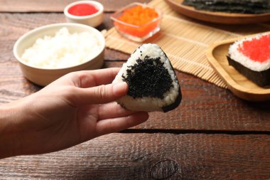 Ahşap masada lezzetli tobiko onigiri (Japon pirinç topları) olan kadın, yakın plan.