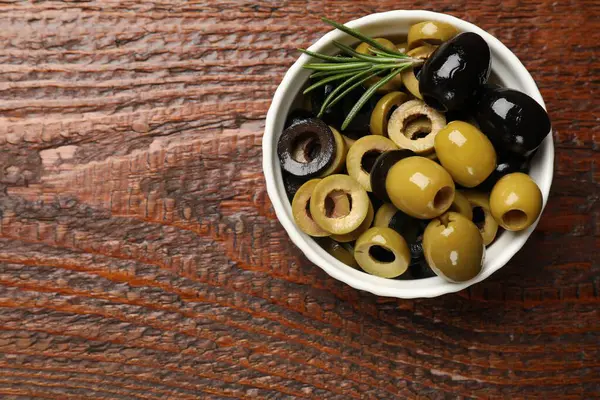 Farklı lezzetlerde marine edilmiş zeytin halkaları, hepsi ve ahşap masada biberiye, üst manzara. Metin için boşluk