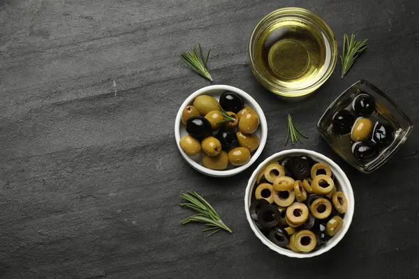 Farklı lezzetlerde marine edilmiş zeytin halkaları, bütün halkalar, koyu dokulu masa üzerinde yağ ve biberiye, düz yatak. Metin için boşluk