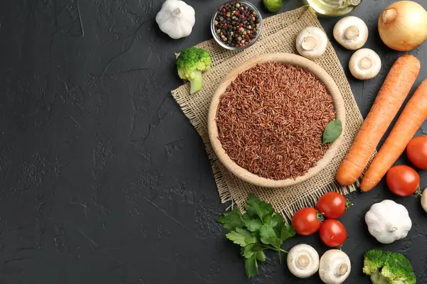 Tabaktaki çiğ kahverengi pirinç taze ürünlerin arasında koyu dokulu masada, düz yerde. Metin için boşluk