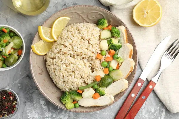 Gri desenli masada servis edilen tavuk, sebze ve limon dilimli lezzetli kahverengi pirinç.