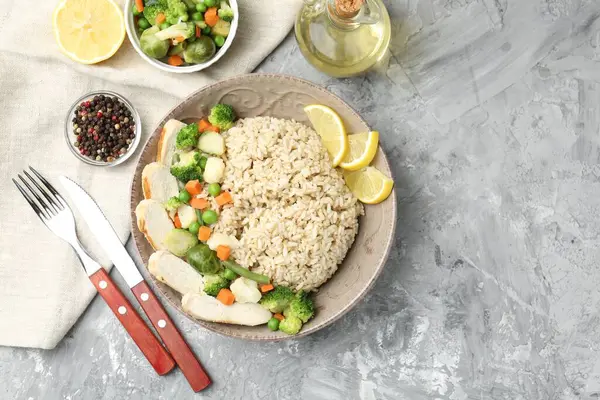 Gri desenli masada servis edilen tavuk, sebze ve limon dilimli lezzetli kahverengi pirinç. Metin için boşluk