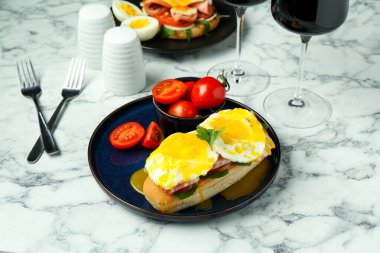 Lezzetli bir kahvaltı. Haşlanmış yumurta, pastırma, çörek ve domates beyaz mermer masada servis edilir.