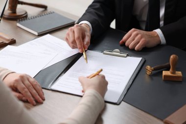 Belgeye işaret eden noter ve müşterinin masa içine imza koyması, yakın plan