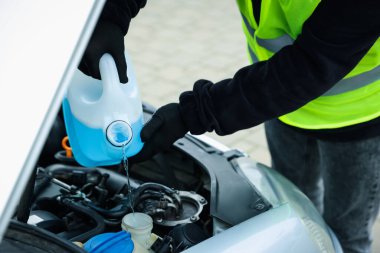 Plastik kutudan araba deposuna cam temizleyici döken bir adam var.