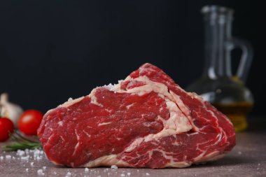 One piece of raw beef with salt on brown textured table against black background, closeup