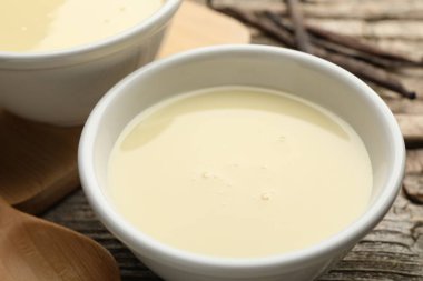 Tahta masadaki lezzetli konsantre süt, kaşık ve vanilya kapsülleri, yakın plan.