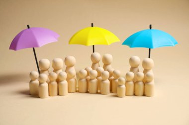 Bej arka planda şemsiye altında insan figürleri. Sigorta konsepti