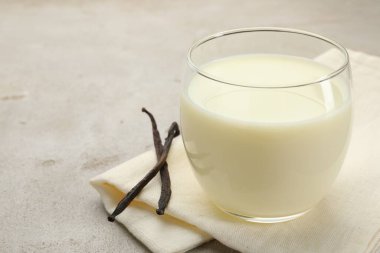 Açık gri masada bir bardak süt ve vanilya kabuğu, yakın plan.