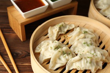 Bambu buharlı buharda kaynamış gyoza (hamur tatlısı), ahşap masada sos ve çubuklar, yakın plan.