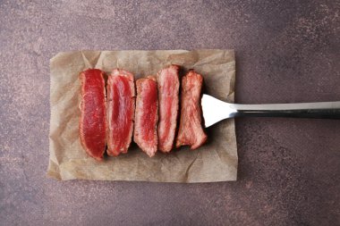 Lezzetli dilimlenmiş sığır filetosu. Kahverengi desenli masa üzerinde farklı derecelerde doness, üst görünüm.