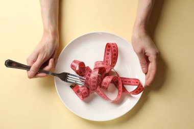 Bulimia. Kadının elinde bej arka planda çatal ve mezuralı bir plaka var.