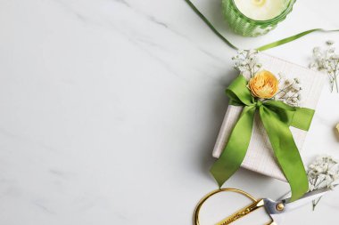 Çiçekçi. Kutu, çiçekler, kurdele, yanan mum ve makas beyaz mermer masada, düz yerde. Metin için boşluk