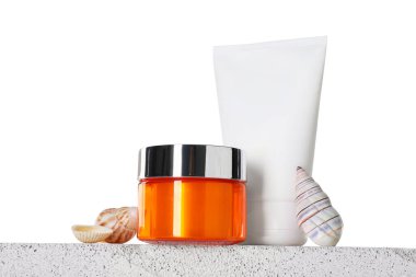 Beton zemin üzerinde beyaz arka plana karşı farklı güneş koruma ürünleri ve deniz kabukları