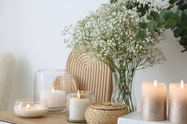 Beautiful gypsophila flowers, eucalyptus branches and burning candles on commode at home