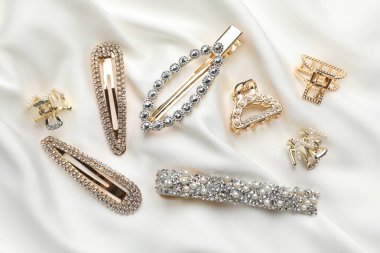 Beautiful hair clips on white silk fabric, flat lay