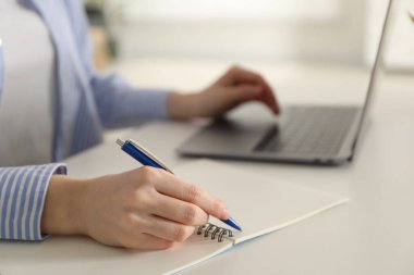 Beyaz masa içerisindeki çevrimiçi derste not alan bir kadın, yakın plan. Kendi kendine çalışma.