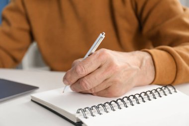 Üst düzey bir adam çevrimiçi olarak masa başında çalışırken notlar alıyor, yakın plan. Kendi kendine çalışma.