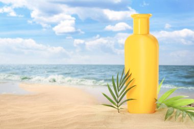 Bir şişe güneş kremi ve okyanus yakınlarındaki kumlu sahilde yeşil tropik yapraklar.