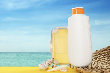 Bir şişe güneş kremi, oyuncak bavul ve okyanus kenarındaki masada deniz kabukları.