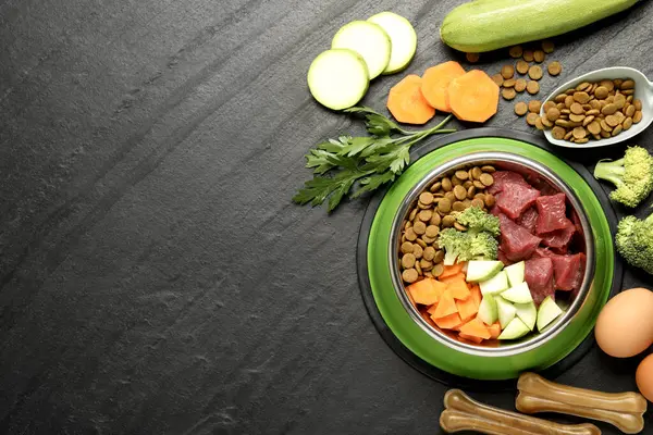 Beslenme kabında doğal ve kuru evcil hayvan mamaları. Koyu dokulu masa üzerindeki ürünler arasında, düz yatak. Metin için boşluk