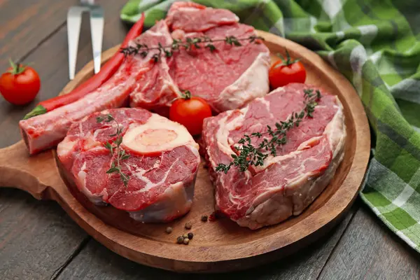 Çiğ et parçaları, domates ve baharatlar ahşap masada, yakın plan.