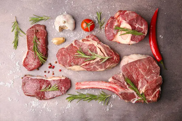 Flat lay composition with pieces of raw beef, salt, rosemary and products on brown textured table