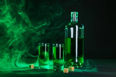 Absinthe shot bardakları, şişe ve esmer şeker siyah arka planda dumanlı
