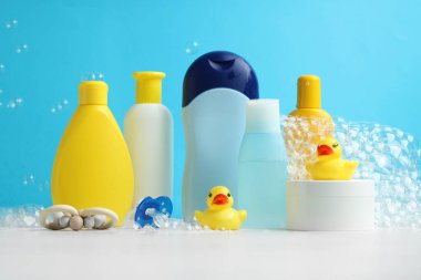 Bebek kozmetik ürünleri, emzik, lastik ördekler ve uçan baloncuklar açık mavi arka plana karşı gri masada