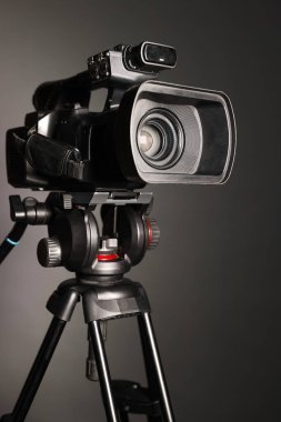 Gri arka planda tripodu olan modern video kamera