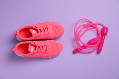 Spor ayakkabılar ve mor arka planda ip atlama, düz yatış. Spor malzemeleri.