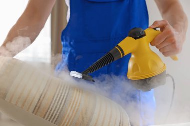 Temizlikçi yastığı evde buhar temizleyicisiyle temizliyor.