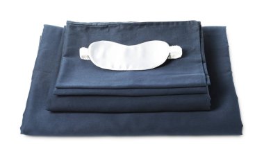 Beyaz arka planda ipeksi çarşaf ve uyku maskesi yığını